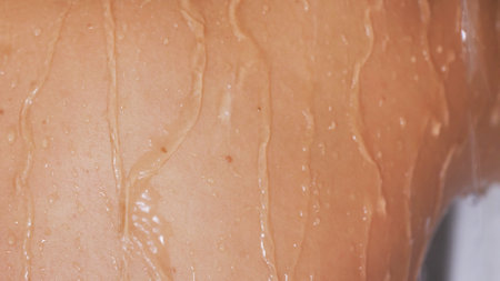Close-up rear view of woman in shower with drops of water running down her wet skin.の写真素材