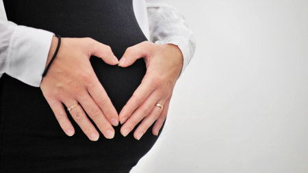 Pregnant Woman holding her hands in a heart shape on her baby bump. Pregnant Belly with fingers Heart symbol. Maternity concept, Baby Showerの写真素材
