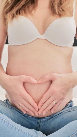 Pregnant woman holding stomach in heart shape gesture with hands on her belly. Pregnancy concept...