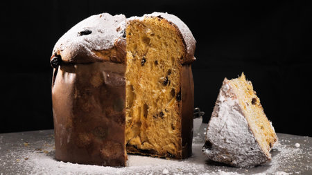 Panettone biscuit with dried fruits on a black background and sprinkled with powdered sugarの写真素材