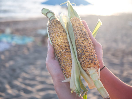 Hot fried corn in a mans hand against the background of the setting sun.の写真素材