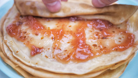 Pancakes are covered with jam, adding, applying pink jam to the French pancakes in the dishの写真素材