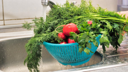 male hands holding plastic colander filled with fresh ripe vegetables and herbs under splashing water above kitchen sink where other vegetables are storedの写真素材