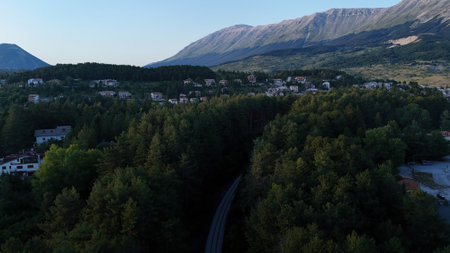 The gentle curves of towering mountains cradle a peaceful valley adorned with dense pine trees. A...