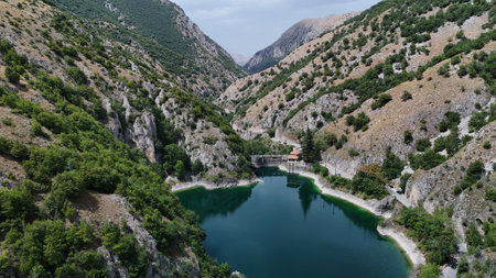 Nestled between towering mountains, the tranquil lake reflects the sky as lush greenery hugs its shores, inviting explorers to discover its beauty.の写真素材