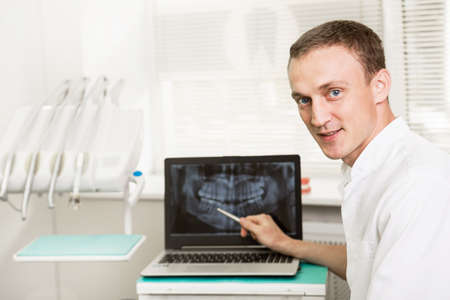 Positive dentist showing on a laptop teeth x-ray picture in dental clinic office. stomatology and...