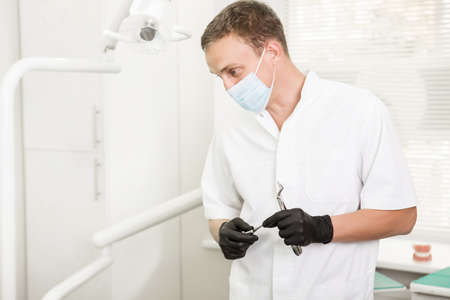 dentist in a medical mask looking looks away, holding a dental pliers