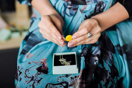 female hands holding beautiful necklace with yellow enamel Jewelry. closeup hands. Fashion accessories for womenの写真素材