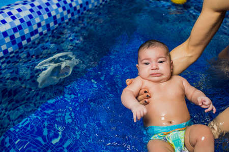 Mother teaching swimming little baby, dressed in swimmer nappies, at swimming pool, top viewの写真素材