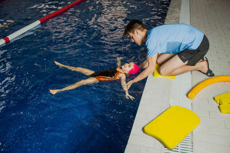 Swimming coach teaches the girl to keep the balance in the water. child floating in the pool