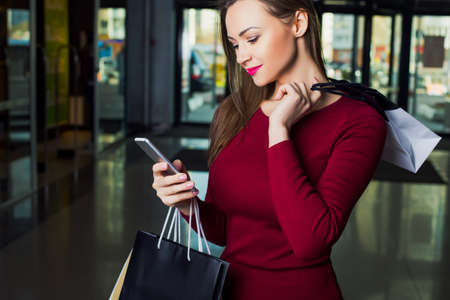 Woman looking in the phone, holding shopping bags while standing in the mall. Shopping lady.の写真素材