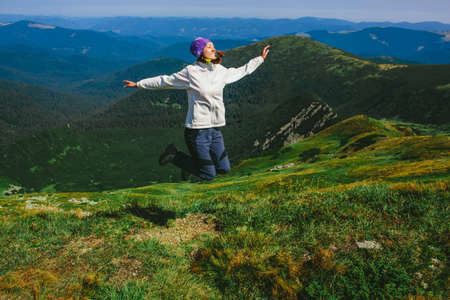 woman traveler jumping against the backdrop of a mountainous landscape. Hiking in the mountainsの写真素材