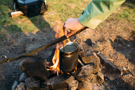 Female's hand holding cast iron pot on a campfire. Cooking at the campfireの写真素材