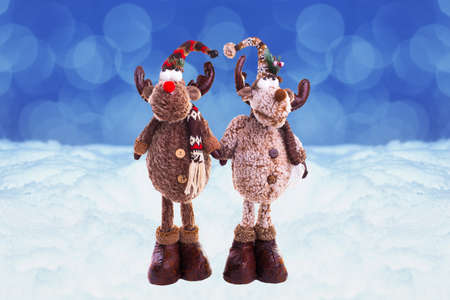 Two toy Elk wearing a knitted hat and scarf. behind them, the snow blurred background. The concept of the winter holidaysの写真素材