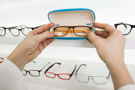 optometrist holding new eyeglass frame, near white showcase with glasses, close-upの写真素材