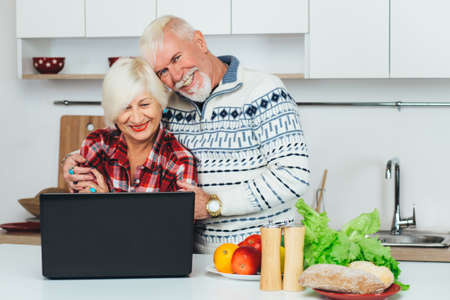 Elderly man and woman are looking for a recipe in a laptop, preparing healthy food at home, in the kitchenの写真素材