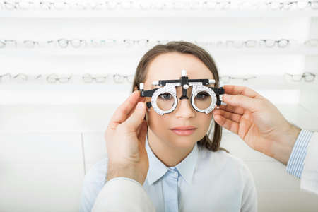 Man ophthalmologist examining patient woman with optometrist trial frame. female patient to check vision in ophthalmological clinic, face close-upの写真素材