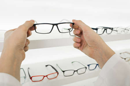 doctors hands holding glasses at optical store, out of focus showcase with many glasses.の写真素材