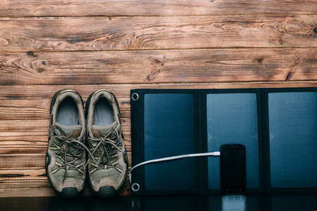 Portable Solar Battery,phone, and trekking shoes - preparing for a hike on wooden backgroundの写真素材