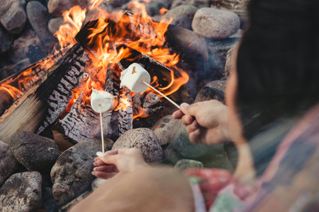 loving couple hands in front of the fire place cooking marshmellow on the lake sideの写真素材