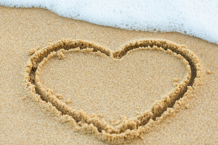 Heart drawn on the beach sand with sea foamの写真素材