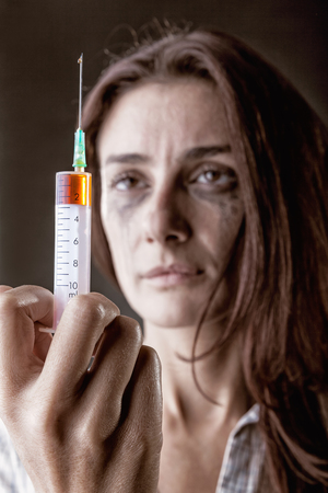 Young woman with drug addiction on dark backgroundÑ Focus on syringeの写真素材