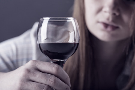 Young beautiful woman in depression, drinking alcohol on dark background