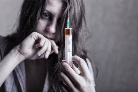 Young woman with drug addiction on dark background. Focus on syringeの写真素材