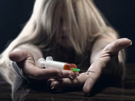 A young woman with a drug holding a syringe on dark background. Focus on handsの写真素材