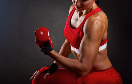 Athletic young woman doing workout with weights on dark background