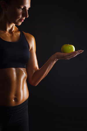 Muscular woman with apple on dark backgroundの写真素材