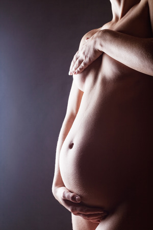 Naked pregnant woman on a dark backgroundの写真素材