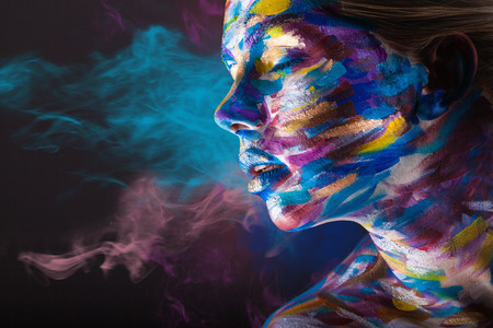 Young woman with colorful make-up and body art on a black with multi-colored smoke