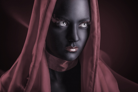 Young woman in a cape with black makeup on a dark の写真素材
