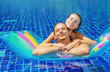 Beautiful young couple bathing in the pool on an inflatable mattressの写真素材