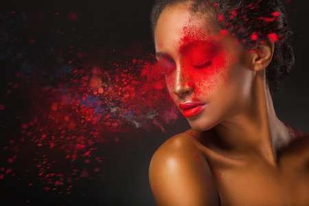 Fashion makeup. Close-up face of a beautiful young woman with splashes of red paint on a black backgroundの写真素材