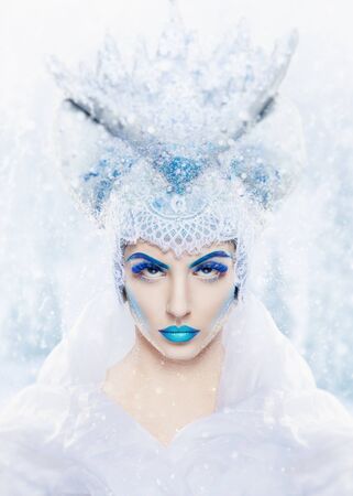 Winter portrait. Fashion makeup. Snow queen with a bright blue make-up on a snowy backgroundの写真素材