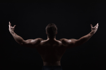 Silhouette. Man shows his muscular back on a dark backgroundの写真素材