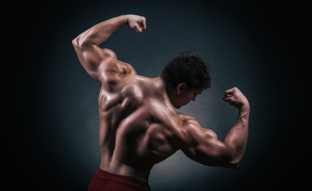Athletic man showing his muscular back and arms on a dark backgroundの写真素材