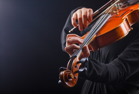 Playing the violin. Musical instrument with performer hands on dark backgroundの写真素材