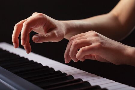 Close-up of a female hands playing piano  on a black background