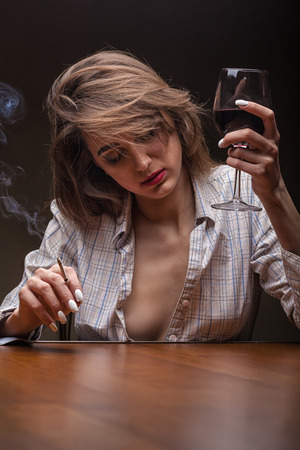 Young beautiful woman is sad with a glass of red wine and a cigarette against a dark backgroundの写真素材