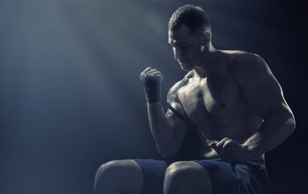 Boxer putting on straps preparing for combat on a dark background