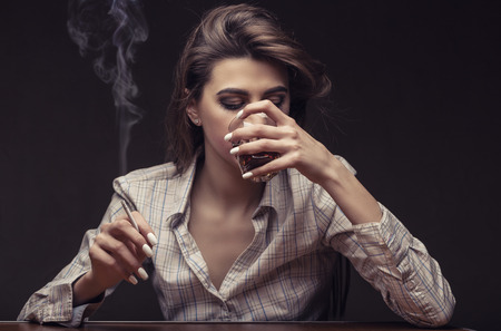 Young beautiful woman is sad with a glass of red wine and a cigarette against a dark backgroundの写真素材