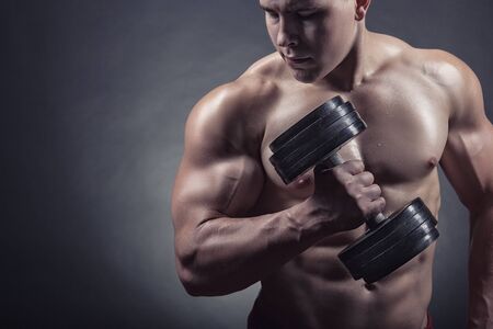 Fit muscular man exercising with dumbbell on dark background
