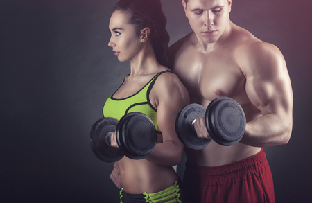Fitness couple exercise with dumbbells on a black backgroundの写真素材