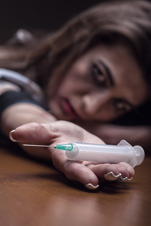 A young woman with a drug holding a syringe on dark background. Focus on handsの写真素材