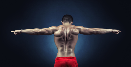Athletic man shows his muscular back on a dark backgroundの写真素材