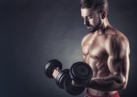 Handsome muscular man exercising with dumbbell on dark backgroundの写真素材