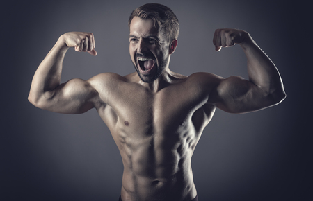 Healthy muscular young man showing his muscles and screaming against a dark backgroundの写真素材